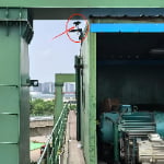 A security camera is mounted on the upper edge of a green industrial building, highlighted by a red circle and arrow. An electric motor is partially visible inside the structure.