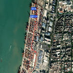 Satellite view of a port with containers, buildings, and a red navigation route marked from a dock to a location labeled with coordinates and text.