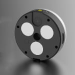 A round, black and white electronic device with four circular sensors, a speaker, a yellow button, and a USB port on the side, shown on a gray surface.