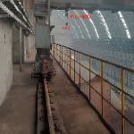 Industrial interior with a rail-mounted machine on a track by a yellow safety railing, concrete walls, and large metal and glass windows. Chinese text is visible in the background.