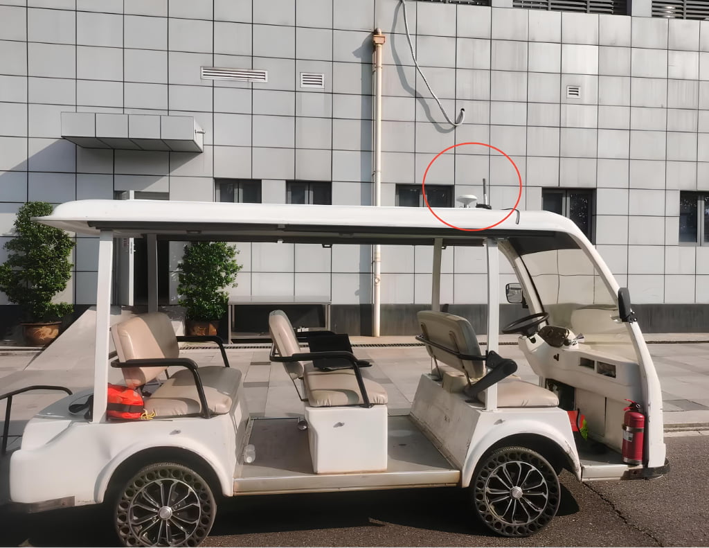 A white golf cart is parked on the street in front of a gray tiled building. A security camera, circled in red, is mounted high on the wall above the cart.