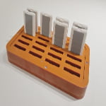 An orange holder with multiple slots contains six white and gray rectangular electronic devices standing upright.