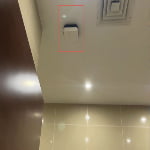 A white sn2-uwb-anchor device is mounted on the ceiling of a room next to a vent and a ceiling light, with a red box highlighting the device.