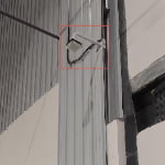 A sn2-uwb-anchor security camera is mounted on a corrugated metal wall, with cables running along the surface and a metal beam visible nearby.