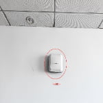 A white electronic device labeled "UWB anchor" (sn2-uwb-anchor) is mounted high on a white wall below a suspended ceiling with visible panels and a light fixture.