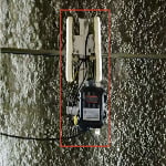 A wireless communication device with two antennas is mounted on a textured concrete wall, enclosed by a red rectangle.