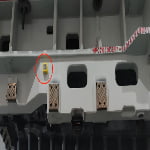 Large industrial machine part with several rectangular metal components; a small yellow device is attached and circled in red near the top left.